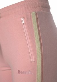 Helle rosa Jogginghosen mit einem seitlichen Reißverschluss und vertikalen Streifen in Beige und Braun, mit dem "Bench."-Logo in glitzerndem Text.