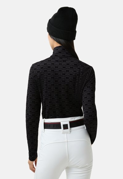 Μαύρο τοπ με ψεύτικο λαιμό και υφασμένο σχέδιο, συνδυασμένο με λευκό παντελόνι και μαύρο πλεκτό σκουφάκι. Διαθέτει λεπτομέρεια ζώνης σε αντίθετο χρώμα.