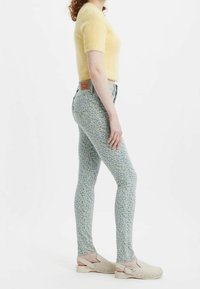 Jeans de lavado azul claro con estampado floral, de cintura alta y corte ajustado, combinados con un suéter amarillo de manga corta y textura suave, y zuecos beige.