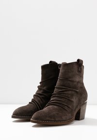 Botines de ante marrón con un diseño arrugado, punta redonda y tacón apilado. Cuenta con un cierre de cremallera y una pequeña lengüeta.