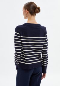 Marineblauer Pullover mit cremefarbenen horizontalen Streifen, geripptem Kragen und Saum, gestrickter Textur, lockerer Passform und Raglanärmel.