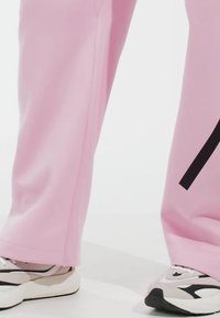 Ljust rosa sweatpants i mjukt material med rak ben-design och svarta accentremsor, kombinerat med kraftiga svarta och vita sneakers.