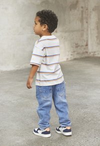 Randig, kortärmad T-shirt i vitt med orange och blå linjer. Blå denimjeans med bakfickor, i kombination med vita och marinblå sneakers.