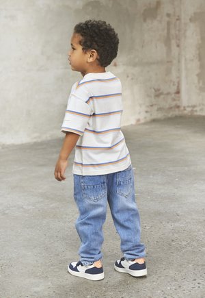 Pasiasta, krótki rękaw T-shirt w białym kolorze z pomarańczowymi i niebieskimi liniami. Niebieskie dżinsy z tylnymi kieszeniami, w połączeniu z białymi i granatowymi trampkami.