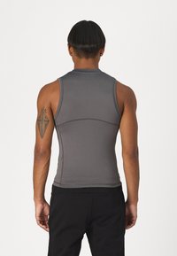 Débardeur de sport sans manches en tissu gris foncé, présentant une texture lisse, un design ajusté et des coutures contrastantes le long des démarcations.