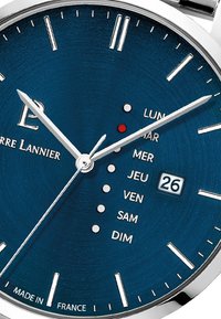 Reloj con esfera azul y marcadores de hora plateados, display de fecha y manecillas plateadas. Presenta indicadores de día de la semana en texto blanco. Fabricado en Francia.