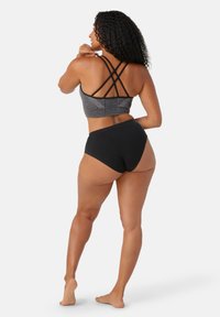 Svart sport-bh med korsade ryggband och geometriskt mönster, ihopparad med högmidjade svarta trosor, uppställd mot en vit bakgrund.