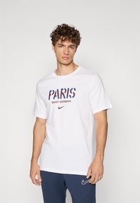 Baltas medvilninis marškinėliai su mėlynu ir raudonu raštu užrašu "PARIS", "SAINT-GERMAIN" raudonai rudos spalvos ir mažu raudonu Nike logotipu apačioje.
