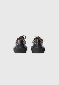Chaussures en cuir noir avec une semelle épaisse et des éléments décoratifs, comprenant des lacets et une texture lisse, vues de l'arrière.