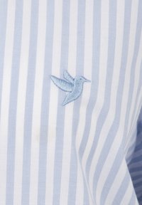 Helleblau- und weiß gestreifter Stoff mit einem kleinen, in hellblau gestickten Kolibri. Glatte Textur mit einem subtilen Glanz.
