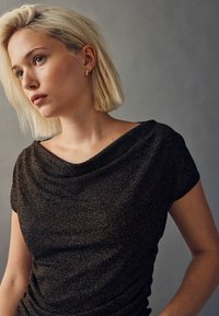 Sort, glitrende top med draperet hals og korte ærmer. Har en blød tekstur og tætsiddende design, accentueret med sammenfoldet detalje.