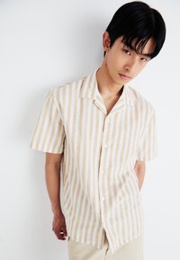Camisa de botones de manga corta a rayas en beige y blanco. Confeccionada en una tela ligera, con un collar clásico y un corte relajado.