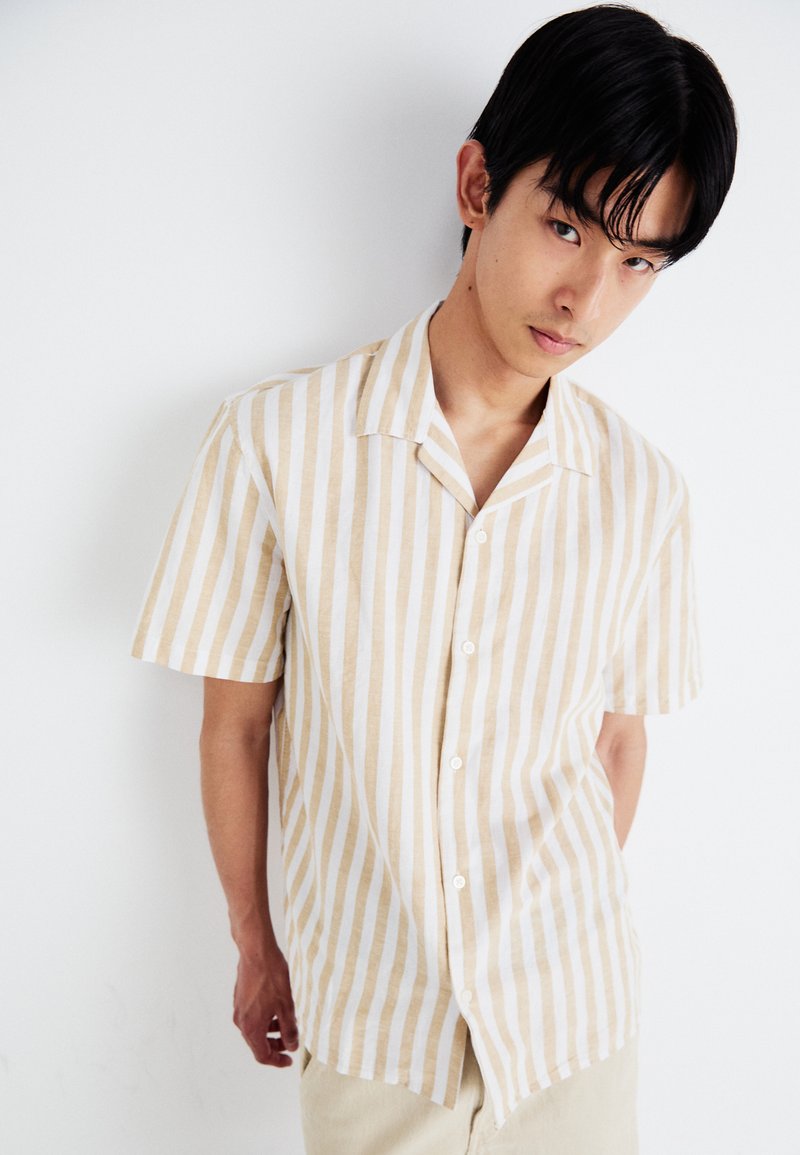 Camisa de botones de manga corta a rayas en beige y blanco. Confeccionada en una tela ligera, con un collar clásico y un corte relajado.