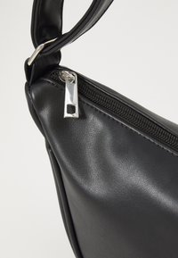 Melnā mākslīgās ādas rokassoma ar rāvējslēdzēja aizdari, noapaļotu formu un plakanu siksnu. Satur metāla rāvējslēdzēja vilkšanas elementu un gludu tekstūru.