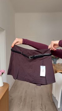 Bordo suknja s prugama s crnim remenom. Ima naborani dizajn i pričvršćenu oznaku. Izrađena od tkanine glatke teksture.