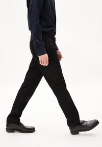 Zwarte jeans hebben een recht gesneden ontwerp met een licht vervaagde textuur. Gecombineerd met glanzende zwarte schoenen en een donker shirt met lange mouwen.