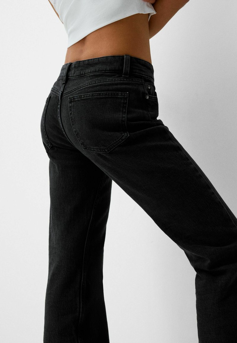 Jeans a campana in denim nero con un design a cinque tasche. Presentano una cucitura sottile e una vita alta, evidenziando un tessuto strutturato.