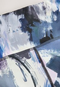 Gros plan d’un tissu avec des coups de pinceau abstraits bleus, blancs et noirs et le mot « ACTIVE » près des coutures cousues.