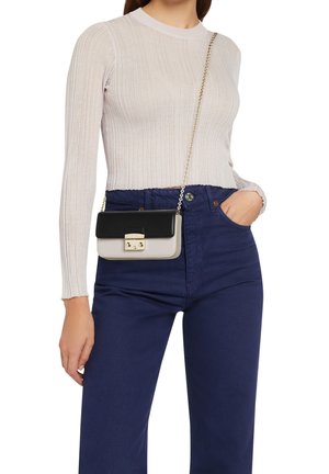 Woman wearing a light beige ribbed long-sleeve top, high-waisted navy blue pants, and a small black and white crossbody bag with gold chain strap.