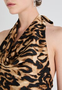 Beige og svart silkeflontrøye med leopardmønster, med en drapert halslinje og strukturert stoff, kombinert med sølv smykker.