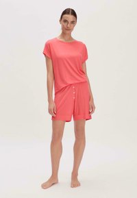 Leichtes, korallenfarbenes Loungewear-Set bestehend aus einem kurzärmligen Oberteil und Shorts mit Knopfverschluss. Weicher Stoff, lockere Passform und glatte Textur.