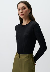 Zwart geribbeld langemouwen shirt met een ronde hals, gecombineerd met olijfgroene satijnen broek, met een zachte textuur en een op maat gemaakte pasvorm.