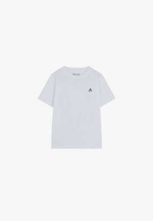 Camiseta blanca de manga corta hecha de algodón, con un pequeño logo de calavera negra en la parte izquierda del pecho. Cuello redondo y corte relajado.
