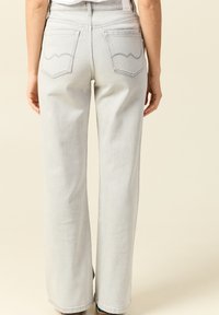 Jeans de mezclilla de corte amplio en gris claro, con dos bolsillos traseros que presentan un patrón de costura ondulada y un diseño de cintura alta.