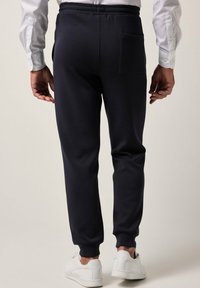 Granatowe spodnie dresowe wykonane z miękkiego materiału, z tapered design, elastycznym pasem i tylną kieszenią. Połączone z białymi trampkami.