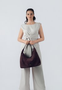 Bolso hobo de ante marrón con una textura suave y forma semiestructurada. Presenta un exterior liso y un asa redondeada.