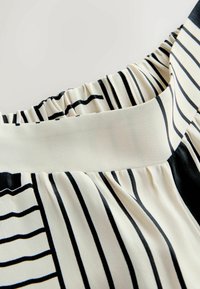 Krupan plan crno-bijele tkanine s naboranim elastičnim pojasom i glatkim dijelom pojasa.