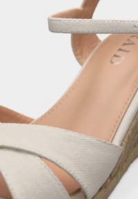 Sandale compensée espadrille beige avec brides en tissu croisées et bride autour de la cheville, dotée d'une semelle en jute tressé et d'une semelle intérieure rembourrée.