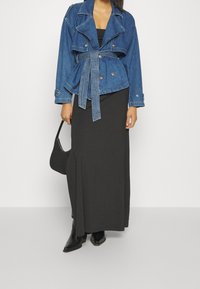 Jeansjacka med bälte vid midjan, mörkblå färg, slagkrage och knapprad, kombinerad med en lång svart kjol och svarta spetsiga stövlar.