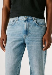 Světle modré džíny z denimu s přímým střihem, zapínáním na knoflíky, bočními kapsami a jemným vyblednutím. Materiál je bavlna s měkkou texturou.