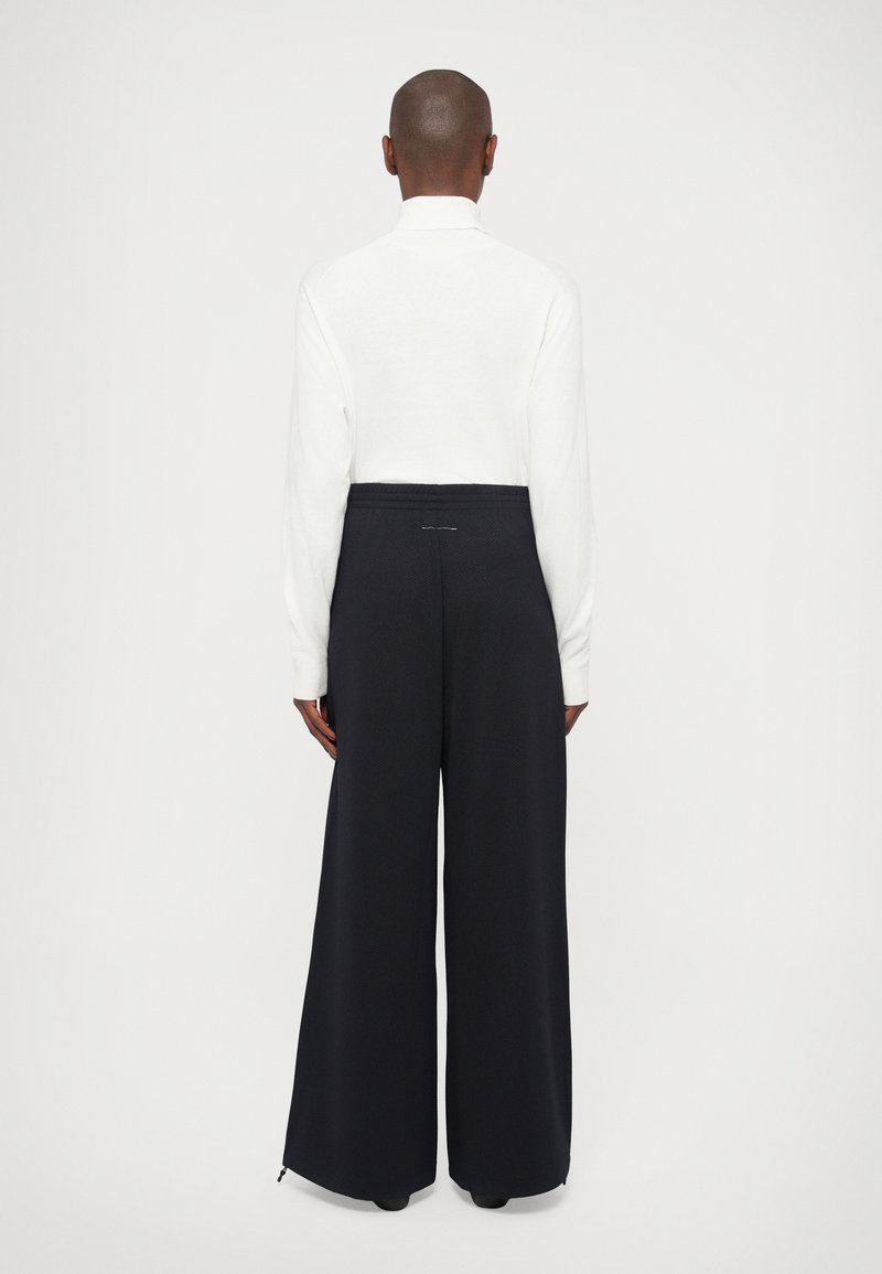 Haut blanc à manches longues et pantalon noir à jambes larges. Le pantalon présente un tissu texturé et une taille élastique. Design simple sans embellissements.