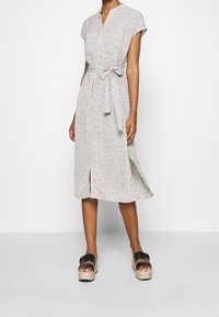 Kukallinen midi-mekko lyhyillä hihoilla, kauluksessa lovi, vyötäröllä sidottu yksityiskohta ja sivuhalkio. Yhdistettynä mustiin platform-sandaaleihin.