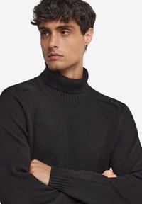 Czarny golf wykonany z teksturowanej dzianiny, z prążkowanymi mankietami i dopasowanym krojem z wysokim kołnierzem.