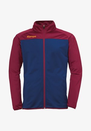 Rode en blauwe ritsjack gemaakt van gladde stof heeft een hoge kraag, lange mouwen en het "Kempa"-logo op de borst.