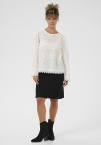 Camicia bianca ricamata con maniche lunghe e pizzo, abbinata a una gonna nera fin sopra il ginocchio e stivali neri con tacco.