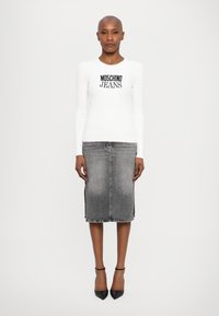 Bela dolga majica z dolgimi rokavi z logotipom "MOSCHINO JEANS", v kombinaciji s sivim denim krilom do kolen, ki ima stranske reze. Črne petke.