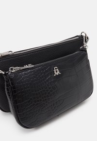 Dvě černé kabelky na ucho se stříbrnými zipy; přední taška má krokodýlí texturu a stříbrný emblém, zadní taška má texturu z jemné kůže.