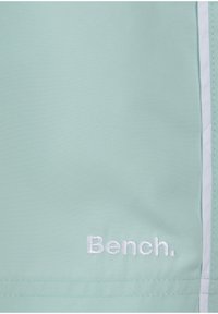 Gaiši zaļš audums ar gludu tekstūru, kam ir baltas akcentas un izšūts "Bench." logo. Vienkāršs un funkcionāls dizains.