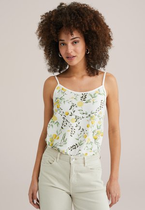 Top bianco senza maniche con stampa di limoni gialli e foglie verdi, spalline sottili e regolabili, tessuto leggero, abbinato a jeans chiari.