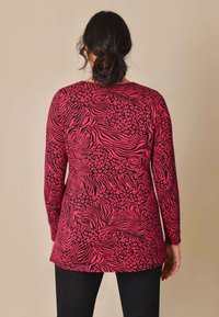 Maglietta a maniche lunghe di un vivace rosa con motivi a zebra e leopardo neri, caratterizzata da un collo rotondo e una vestibilità dritta, realizzata in un materiale morbido.