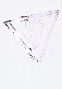 Camiseta blanca con un gráfico que presenta un diseño triangular contorneado con lentejuelas coloridas, mostrando "GUESS U.S.A. WASHED JEANS" en texto en negrita.