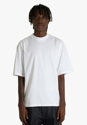 Maglietta bianca a maniche corte in cotone, con scollo rotondo e vestibilità rilassata. Texture liscia senza motivi o dettagli visibili.