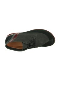 Grijze suède schoen met zwarte leren neuskap, gebogen ontwerp, vetersluiting en contrasterende rode leren accenten aan de zijkant.