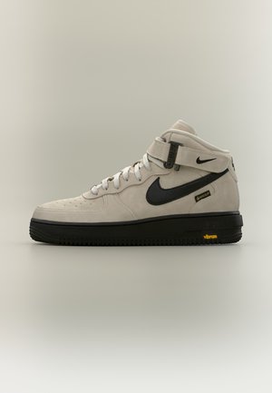 Кремава висока маратонка Nike с черен знак Swoosh, каишка около глезена и дебела черна подметка, показана на изчистен фон.