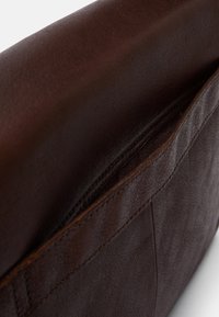 Brązowa skórzana torba o fakturowanej powierzchni, z klapą zamykaną na zatrzask i widocznymi detalami szycia. Kompaktowa konstrukcja z jedną kieszenią.