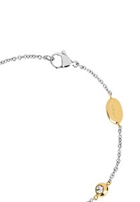 Pulsera de cadena de plata con un acento dorado y cierre, que presenta un colgante circular con un detalle de cristal, eslabones texturizados y un logo grabado.